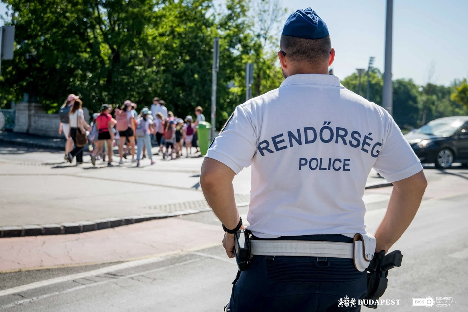 Gyerekcsoport halad át egy zebrán a Hősök terénél egy rendőr felügyelete mellett